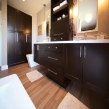 double vanity built of black shaker cabinets has floating vanity sections with drawer base between and wall of storage cabinets with bamboo floor and contemporary toilet and freestanding tub