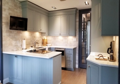 Open U-shaped light blue-gray inset shaker kitchen with peninsula storage, a TV, and buffet storage on opposite side