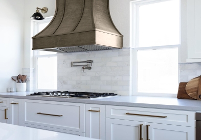 Curved wood range hood with strapping in ash-brown stain against white shaker kitchen cabinets