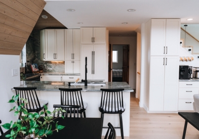 White shaker kitchen cabinet design with black cabinet pulls, light wood accent paneling and stone slab backsplash