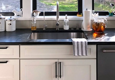 The white Shaker cabinets in this farm kitchen contrast perfectly with the black trimmed windows, countertop and cabinet hardware