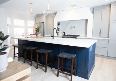 Large one-wall kitchen design with tall light gray shaker kitchen cabinets and gold cabinet hardware with a long dark blue kitchen island and white quartz countertops