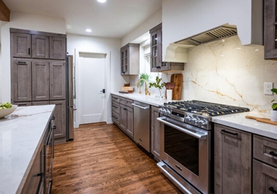 Light gray-brown stained kitchen cabinets with mullion doors, cream countertops, and a slab backsplash