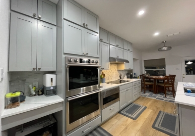 Light gray stacked shaker kitchen cabinets and island with white quartz countertops, brushed nickel cabinet hardware and modern pendant lighting