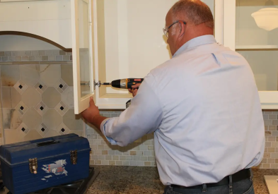 Man installing a glass wall cabinet door in a white shaker kitchen