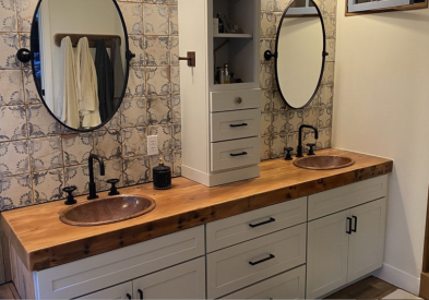 Farmhouse double vanity with soft gray shaker bathroom cabinets, a butcher block countertop, and tall wall cabinet in the center