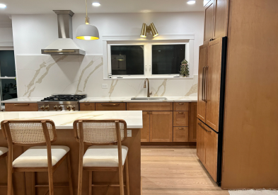 Shaker kitchen design with stained brown cabinets, a paneled refrigerator and large island full of drawers.