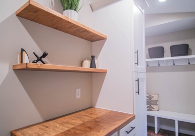 White laundry and mudroom cabinets with warm golden wood floating shelves and a mudroom bench