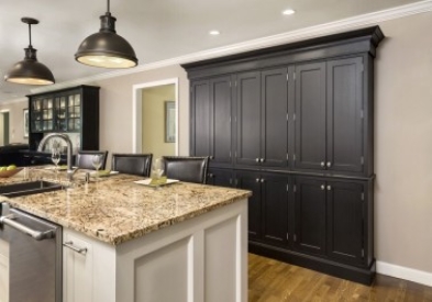 black inset pantry cabinets with exposed nickel hinges next to a white shaker island with golden granite countertops