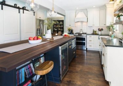 A black island with butcher block counter tops and a built in microwave, bookshelf, and cooler.