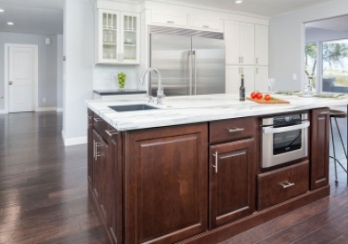 center island built of raised panel cherry cabinets with stainless bar pulls, white marble countertop, prep sink and microwave drawer in kitchen with white shaker perimeter cabinets and hardwood floor