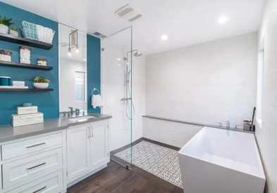 Modern white shaker bathroom cabinets with wood floating shelves next to glass shower and white free-standing tub