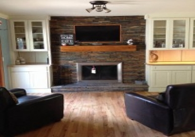 Living room stone fireplace surrounded by white shaker built-in cabinets with glass doors above