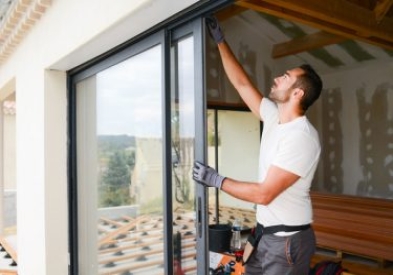 young window installer in white t-shirt putting in a door while remodeling a house