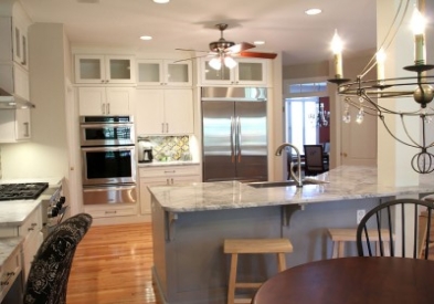 Large stacked white shaker kitchen cabinets with glass on top and kitchen island with white granite countertops