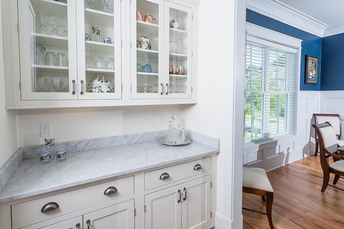 view through the butlers pantry into the adjacent dining area, where the white painted, shaker style architectural style continues with board and batten paneling and wide baseboard