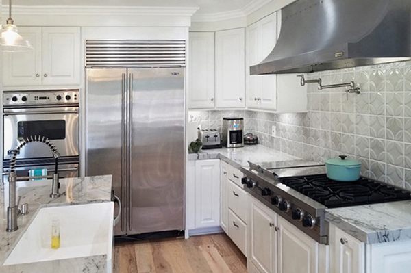 Corner of kitchen with white cabinets, high-end stainless steel appliances and white apron sink in island