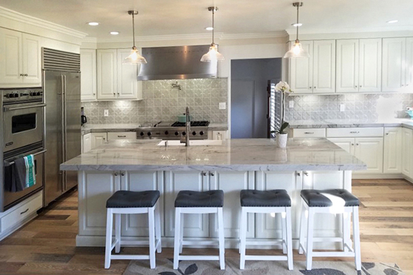 Large kitchen with white cabinets, island with seating, wood floors and professional stainless steel appliances