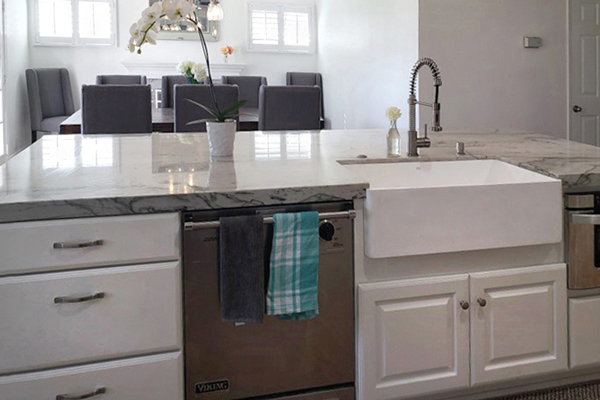 Kitchen island with white cabinets, dishwasher, apron sink and microwave facing the formal dining room