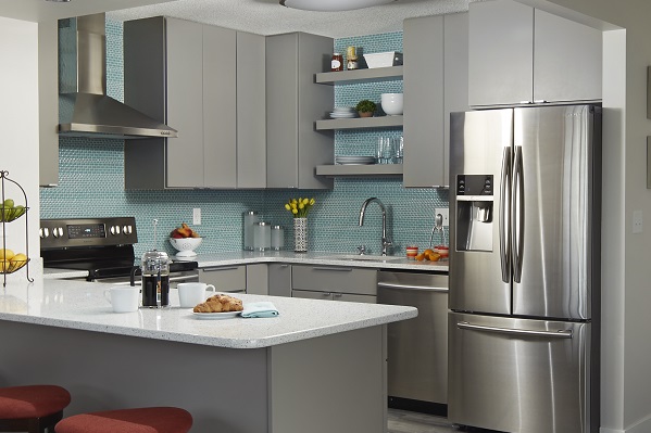 corner view of condo kitchen with gray slab door cabinets, ceiling high aqua glass mosaic tiles, stainless range hood and floating shelves