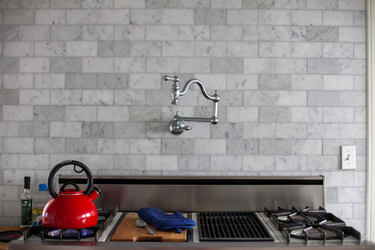 Traditional-style polished chrome pot filler on marble subway tile backsplash over a range