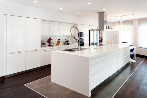 All-white one wall kitchen design with white high-gloss kitchen cabinets, minimal cabinet pulls and a large stainless steel chimney hood over the island