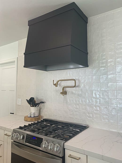 Angled wood range hood in black against white subway tile wall with white shaker base cabinets