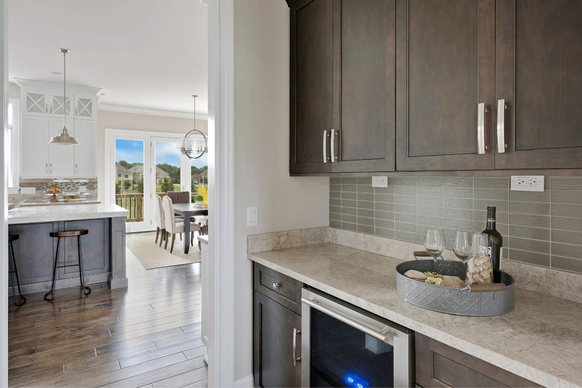 Dark brown stained shaker kitchen cabinets in butler's pantry with cream colored stone countertops