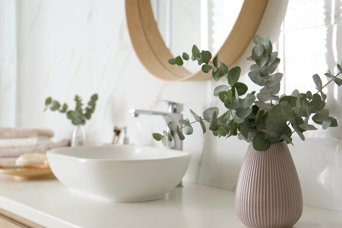 White bathroom vanity countertop and vessel sink next to two eucalyptus plants in ceramic pots