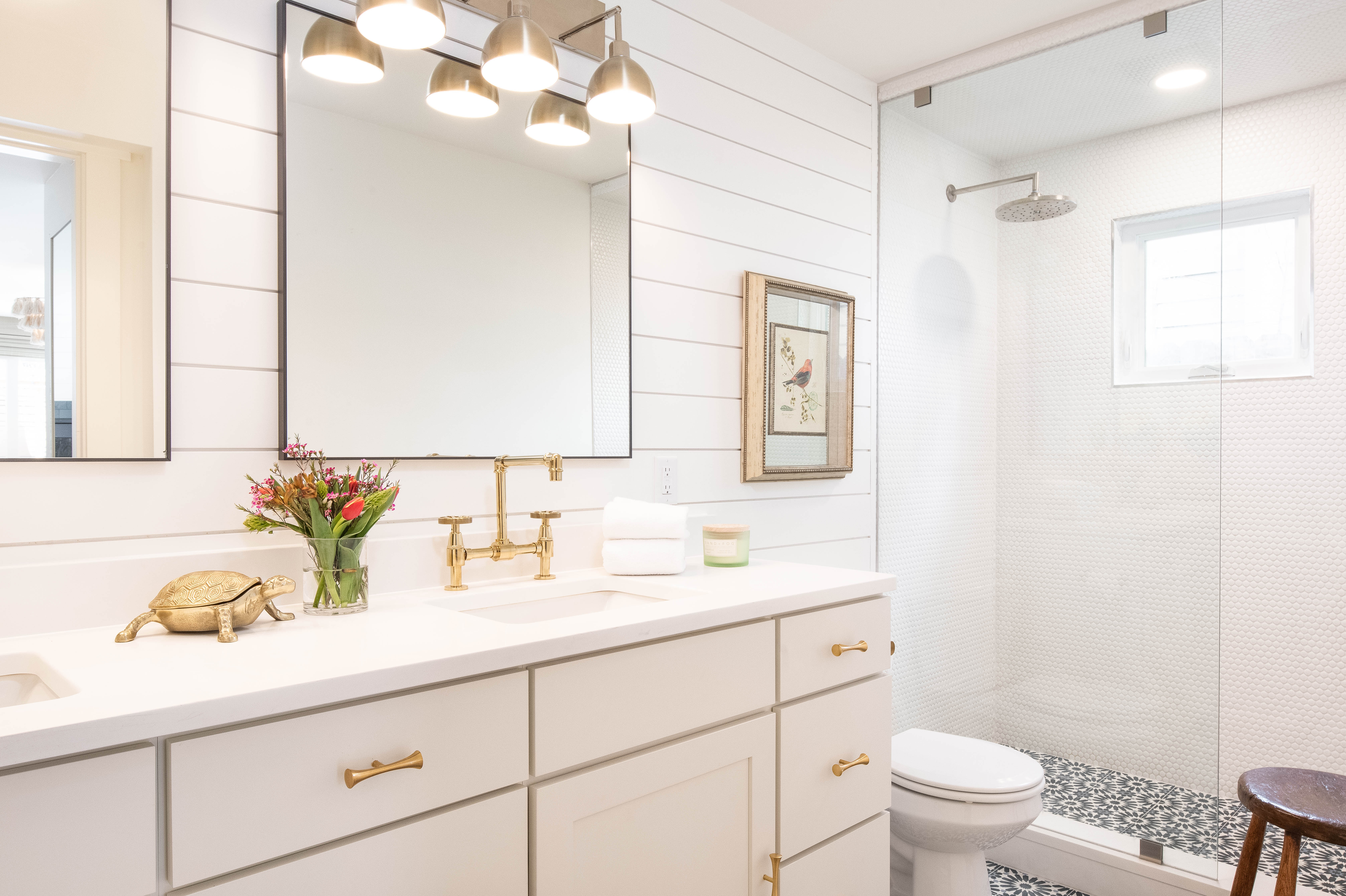 White shaker door double vanity with gold hardware and accents, shiplap white walls, and glass shower enclosure