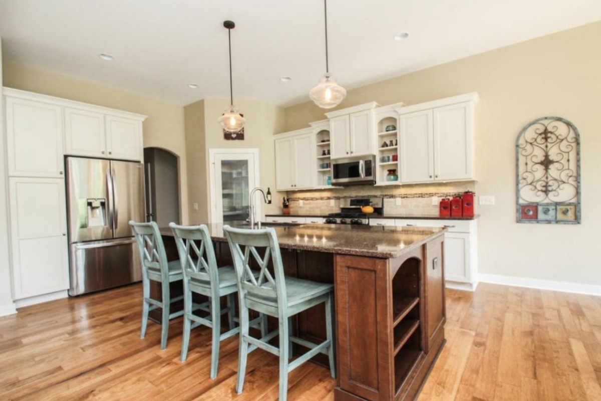 Transitional white shaker kitchen with a cherry shaker island, and blue farmhouse-style chairs for seating