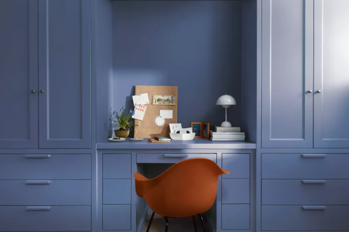 Mid-tone blue wall paint with warm violet undertones and a camel tan chair in front of the built-in desk