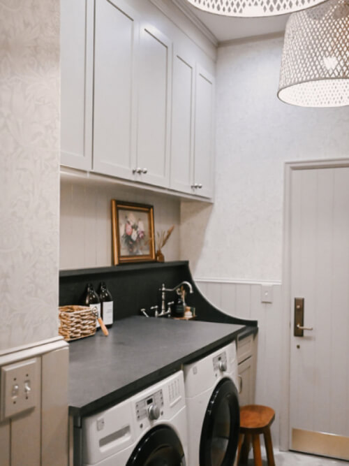 Laundry room wall with white frontloading washer and dryer with black quartz countertops and beige cabinets above