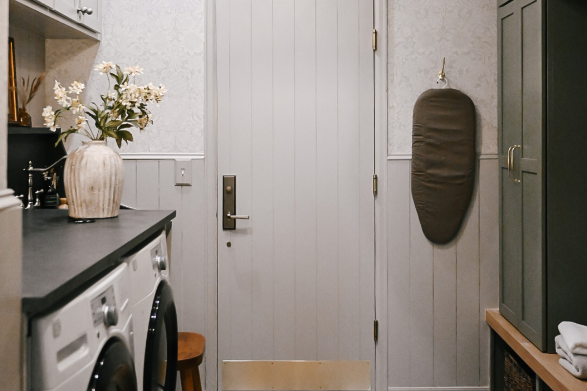 Large luxurious laundry room with taupe laundry cabinets and front load washer/ dryer with olive green mudroom lockers on other side