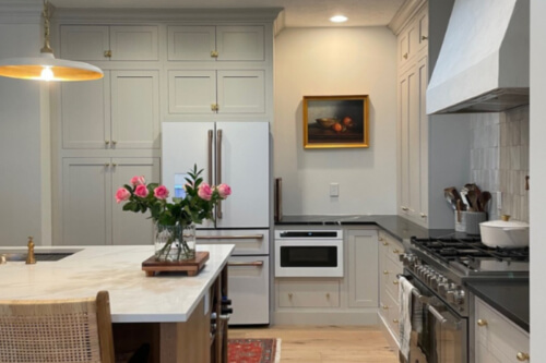 Stacked creme kitchen cabinets in inset style with aged brass cabinet latches, soapstone countertops and a light wood island