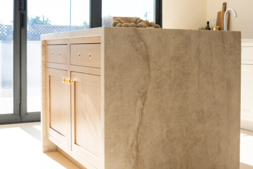 Light oak kitchen island with gold hardware and quartzite waterfall countertop