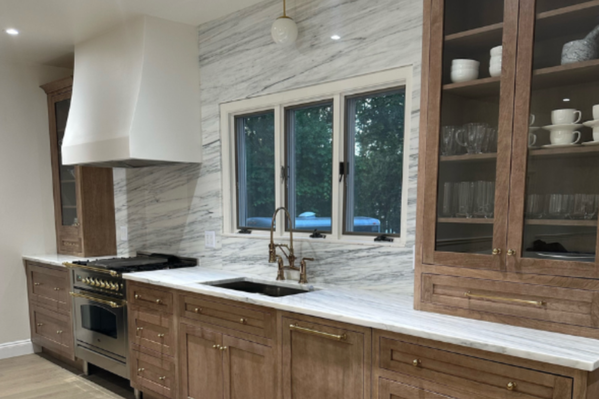 Medium wood tone inset kitchen cabinets with a gas range, white plaster hood and white stone slab covered wall