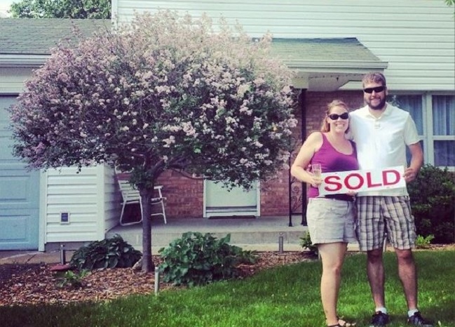 tessa and jake standing in front of house holding a sold sign