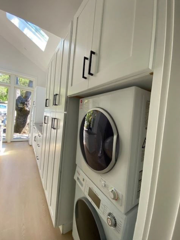 White shaker kitchen cabinet wall with a white front load stackable washer and dryer