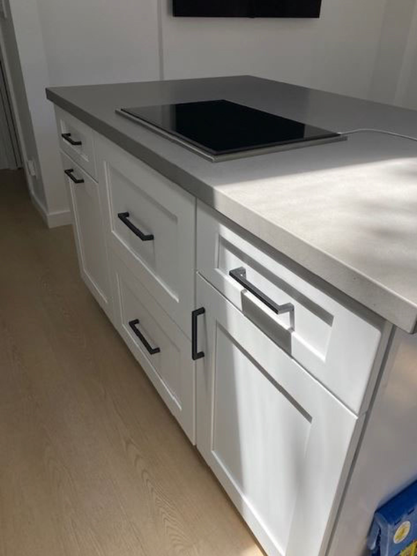 White shaker kitchen island with black cabinet hardware and medium-gray quartz countertops with an integrated cooktop