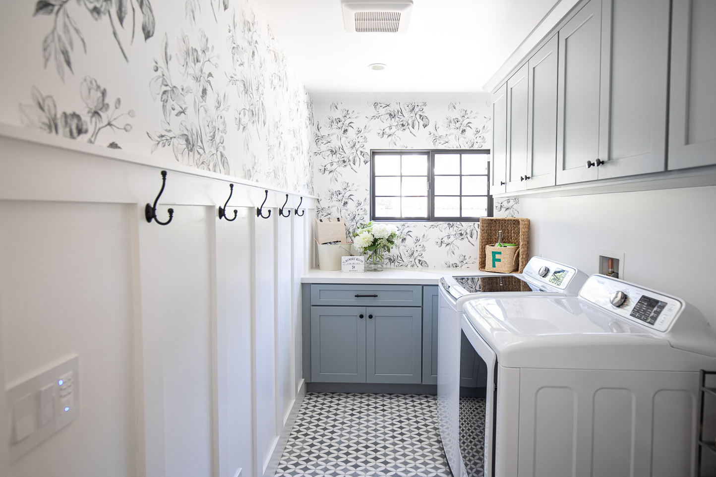 Laundry room cabinets painted a calming shade of blue with floral wallpaper and board and batten trim on the wall.