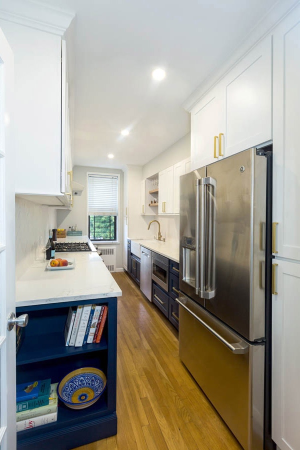 galley kitchen with blue and white cabinets, stainless appliances and gold hardware