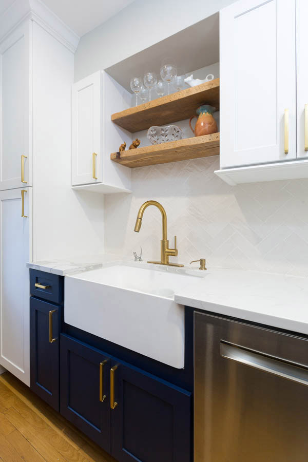 blue sink base cabinet with white apron-front sink, surrounded by white cabinets, stainless dishwasher and wood floating shelves above