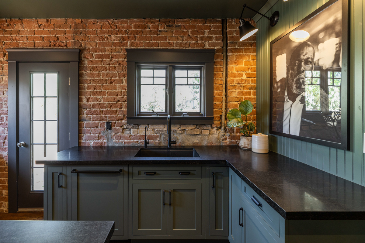 U-shaped large green kitchen with inset cabinets, vintage elements and dark brown island with black granite countertops and hardware