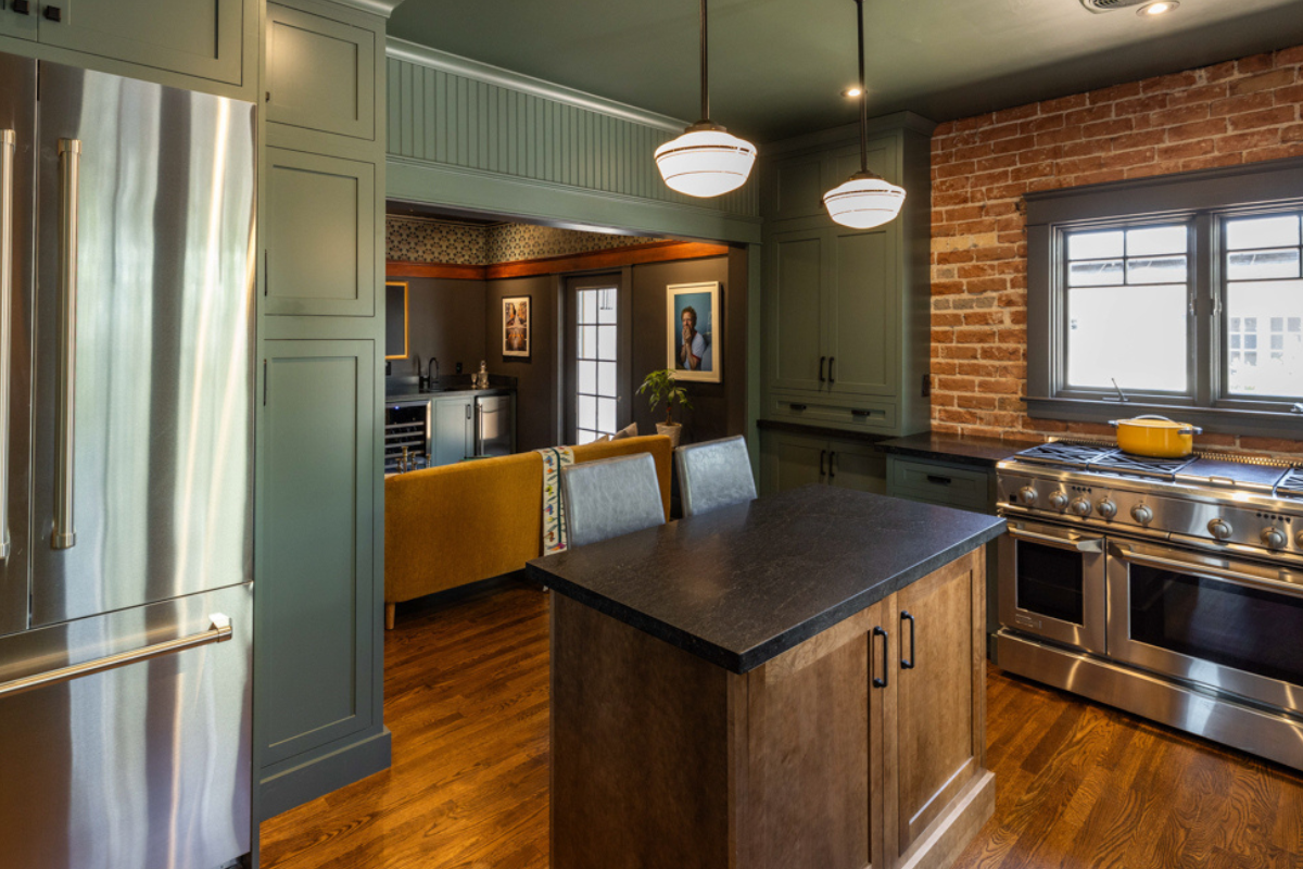 U-shaped large green kitchen with inset cabinets, vintage elements and dark brown island with black granite countertops and hardware