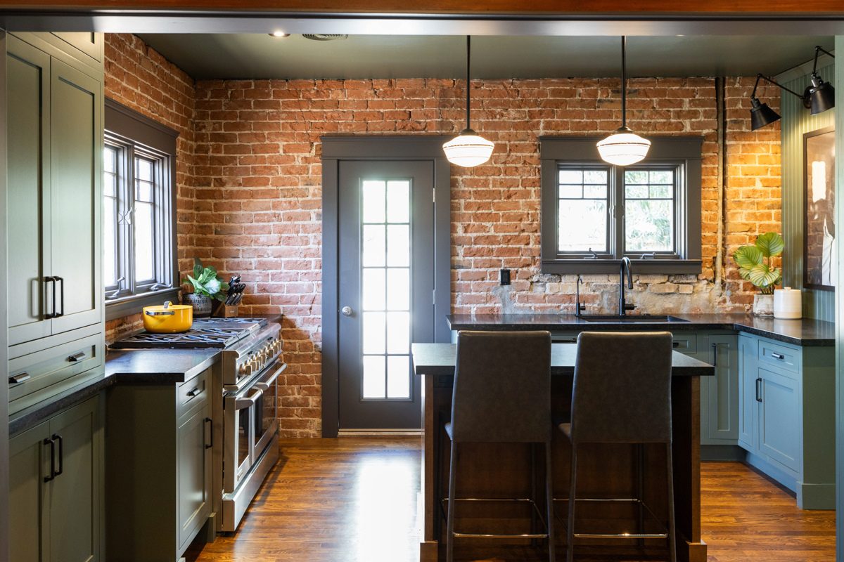 U-shaped large green kitchen with inset cabinets, vintage elements and dark brown island with black granite countertops and hardware