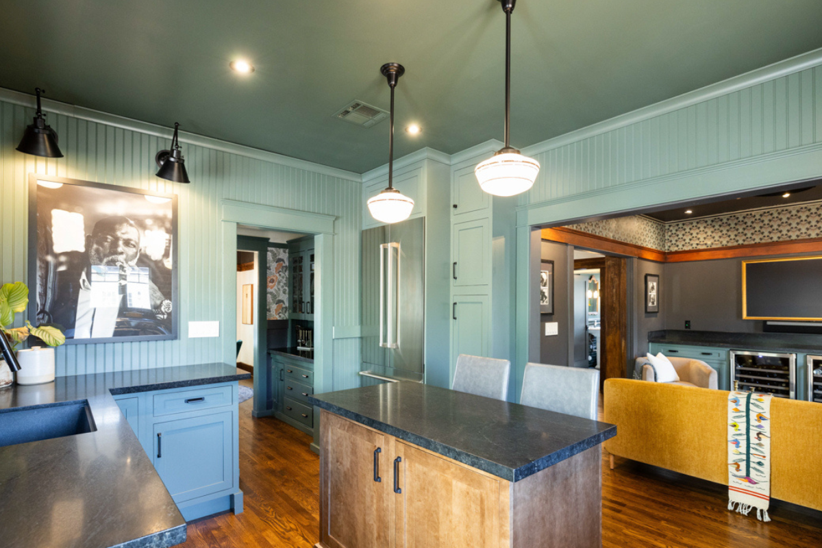 U-shaped large green kitchen with inset cabinets, vintage elements and dark brown island with black granite countertops and hardware