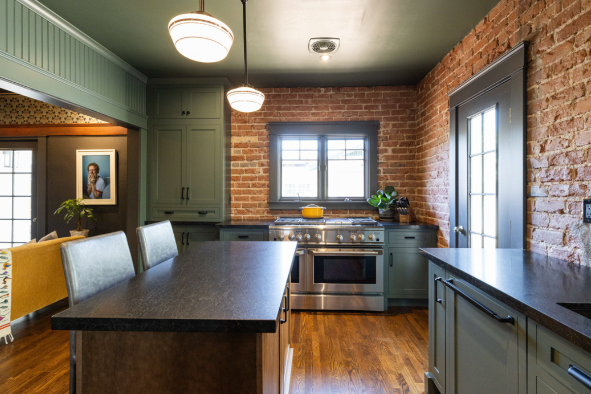 U-shaped large green kitchen with inset cabinets, vintage elements and dark brown island with black granite countertops and hardware