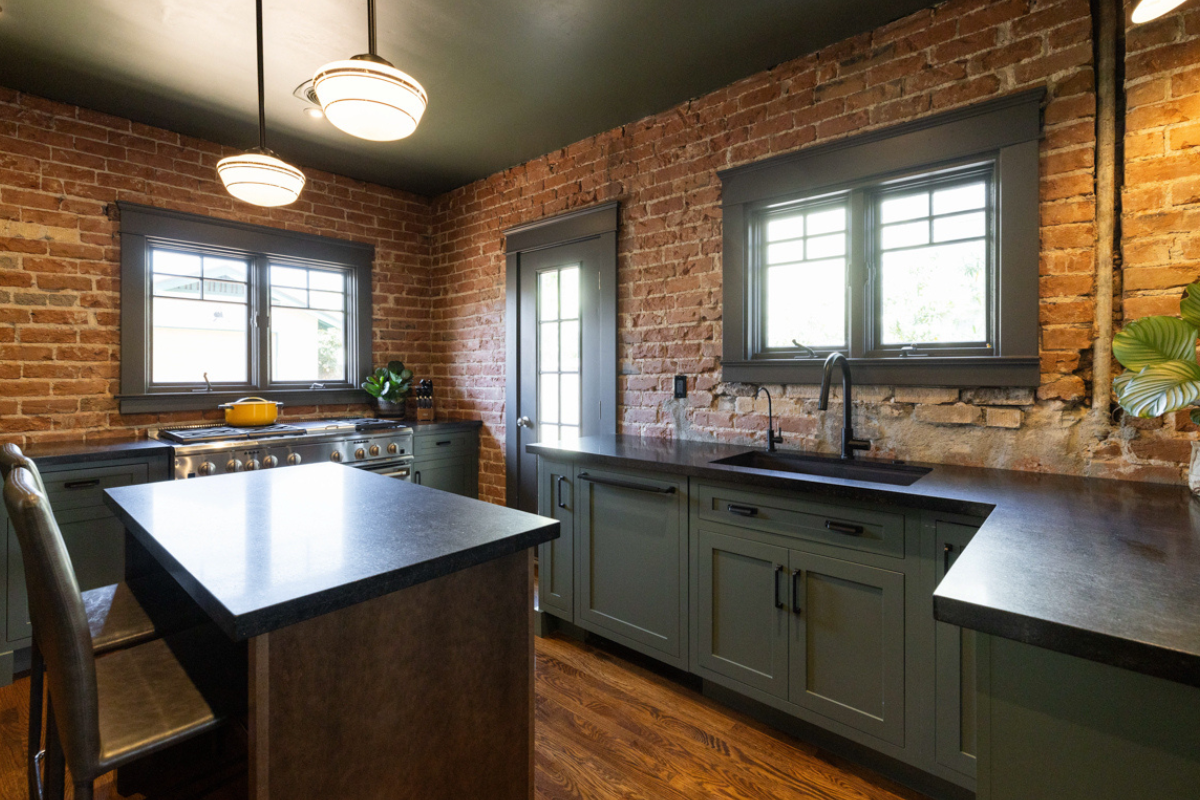 U-shaped large green kitchen with inset cabinets, vintage elements and dark brown island with black granite countertops and hardware