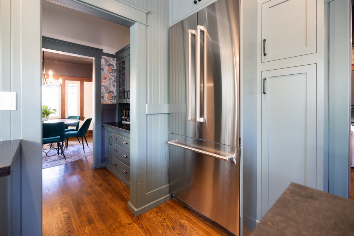 U-shaped large green kitchen with inset cabinets, vintage elements and dark brown island with black granite countertops and hardware